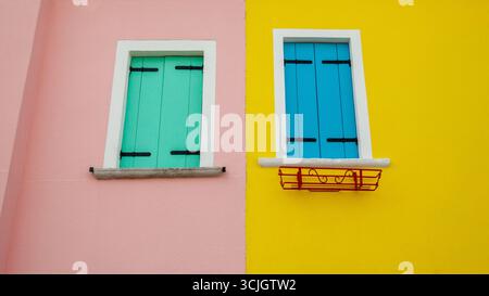 Two windows with green and blue shutters on pink and yellow walls, next door to each other Stock Photo