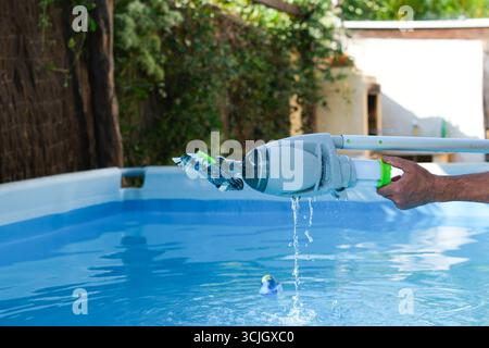 Man Cleaning a Pool in the Yard. Handheld Cordless Rechargeable Pool Vacuum Cleaner with Scrub Brush Head. Water Splashes in Different Directions. Stock Photo