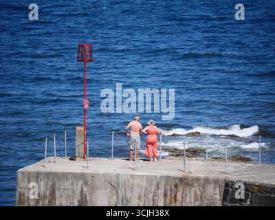 Older couple looking out to sea from a harbour wall on a warm sunny summer day. Cornwall, UK Stock Photo