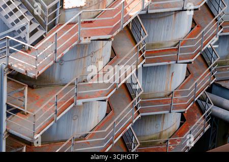 Rusty industrial stairs metal texture pattern. Detailed close-up of symmetrical weathered staircase structures on old factory tanks, perfect as indust Stock Photo