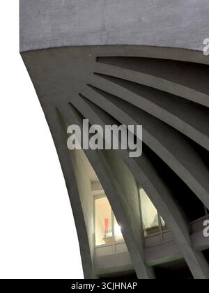 modern concrete structure with bold, curving support fins framing illuminated office windows. The sculptural architectural detail creates a play of li Stock Photo