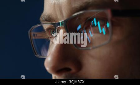 close up of professional trader closely monitors financial analytics, with forex and stock market charts reflected in his eyeglasses, assessing crypto market movements.  Stock Photo