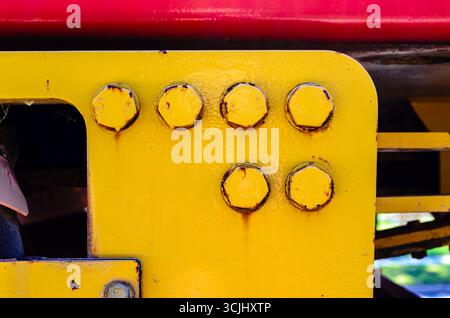 Close-up of six large rusty bolts on a yellow flange showing the old paint and dust bleeding. Stock Photo