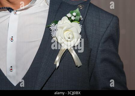 A man in a formal suit with a white beautiful flower boutonniere. Background is softly blurred, suggesting a festive or celebratory atmosphere Stock Photo