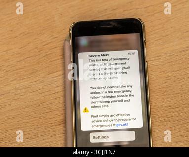 A smartphone displays a UK government test emergency alert notification on a wooden surface Stock Photo
