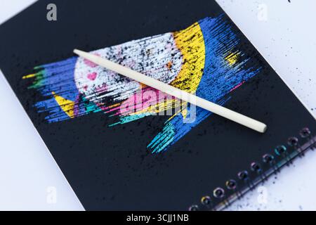 Sketch scraping. A colorful abstract design on a black notebook with a wooden stylus placed on top. Design features vibrant brush strokes Stock Photo