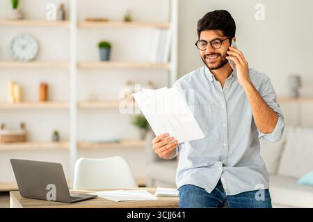 Home office. Confident arab entrepreneur talking with companion on phone and checking financial reports Stock Photo