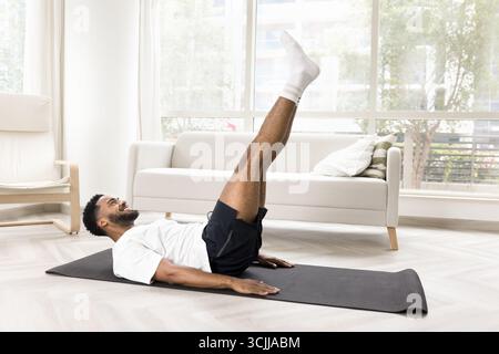 Smiling young man swing press on gymnastic mat at home Stock Photo