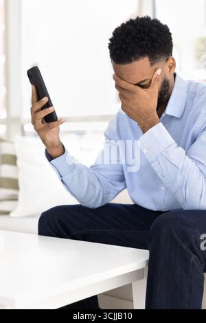 Shocked upset young man holding phone covering face with palm Stock Photo