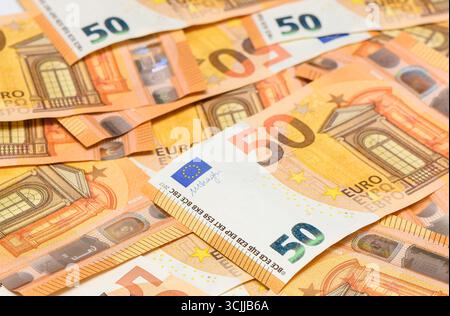 Multiple fifty euro banknotes randomly spread across a table surface, close-up background for financial and economic themes. Stock Photo