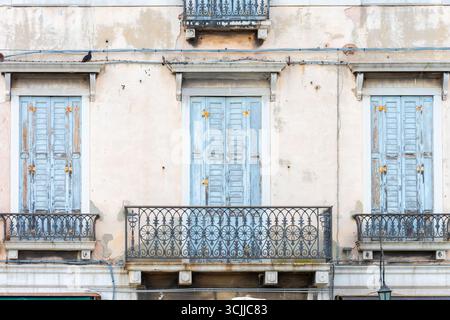 The fa ade of the house with balconies and blue shutters on the windows, with wrought iron railings and peeling plaster Stock Photo