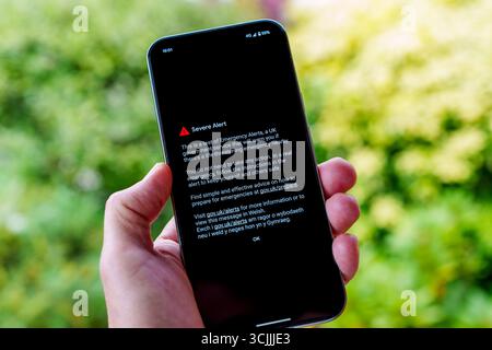 Emergency Alerts UK severe test notification on mobile phone held in a hand outdoors, government life-threatening warning message with red hazard icon Stock Photo