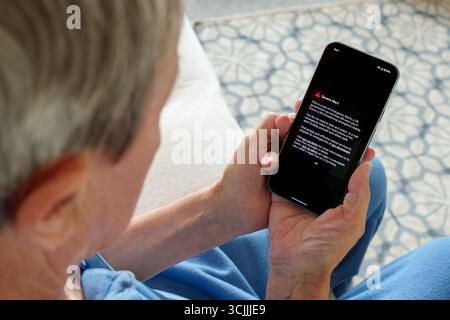 UK Emergency Alert test message displayed on smartphone held by elderly person at home, showing Severe Alert and safety instructions from government. Stock Photo