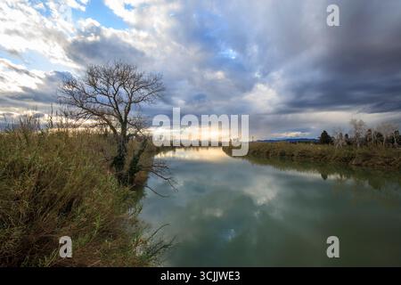 Golden hour over the Ebro: radiant sunlight breaks through dramatic clouds, painting reflections of orange and blue across tranquil waters Stock Photo