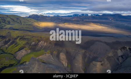 Aerial landscape of Icelandic highlands with volcanic ash slopes green moss patches and golden sunlight breaking through clouds Stock Photo