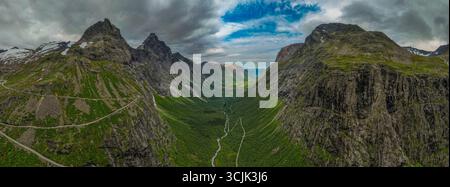 Stunning panoramic view of a deep Norwegian valley framed by steep, green mountains and a vibrant blue sky with clouds Stock Photo