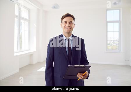 Portrait of young smiling real estate agent man in suit with sale documents looking at camera Stock Photo
