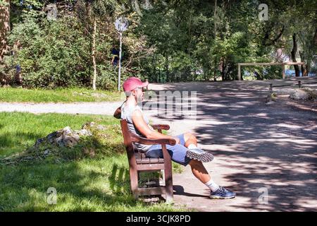 Munich, Germany - September 12, 2018: a runner having a rest sitting on the bench in the park after jogging. Stock Photo