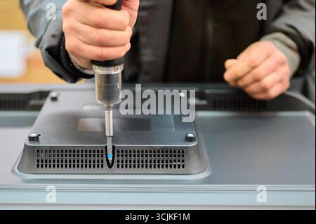 Assembly of television housing at manufacturing facility with technician using screwdriver for installation Stock Photo