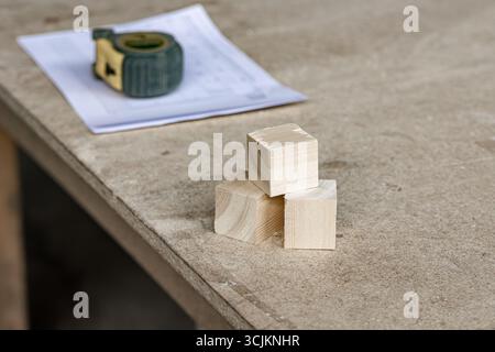 Small wooden cubes made from offcuts placed on a workbench next to a measuring tape and cutting list, indicating efficient material use in woodworking Stock Photo