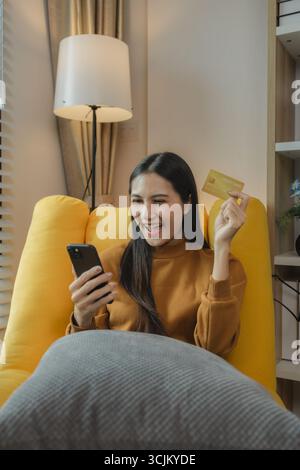 Asian woman sitting on the sofa in the living room, she is shopping online by paying by credit card, shopping on an online shopping platform, paying b Stock Photo