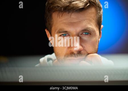 Tired man working at computer in dark room. Close up of man eyes looking at screen. Concept of overwork Stock Photo
