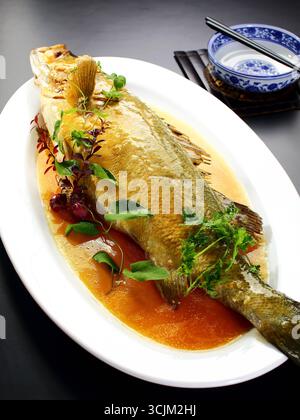 Braised and Pan-Seared Sea Bass in Soy Broth on Oval Platter Stock Photo