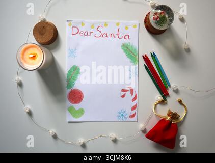 Children's drawing of Dear Santa letter with drawings of fir branches, Christmas ornaments on white surface. Pencils, candle, snow globe, gift bag, st Stock Photo