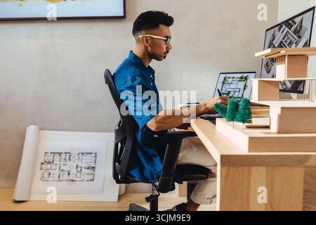 A young architect working diligently in a modern office, designing innovative building models and layouts using a computer and architectural tools, re Stock Photo
