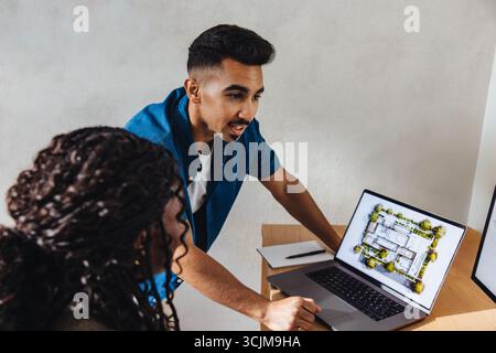 A team of two young professionals in an architecture firm discussing building models on a laptop. The workplace is modern, and they are focused on col Stock Photo
