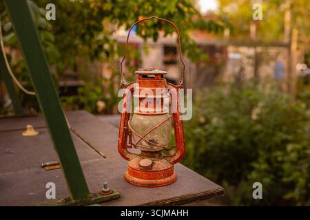 Antique rusty hand-held oil kerosene lantern for old-time lighting. Antique oil lamp outdoors. Collectible tin lamp decoration Stock Photo