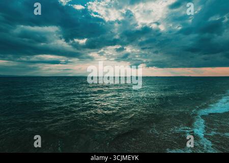 Dark moody seascape with dramatic storm clouds and ocean waves under soft sunset light. Selective focus. Stock Photo