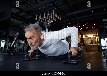 Mature man is doing push-ups in a modern gym Stock Photo