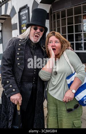 Top hat wearing Count Dracula scaring a woman on the street at Bridport Hat Festival 2025.  Quirky annual summer event in the town. Stock Photo
