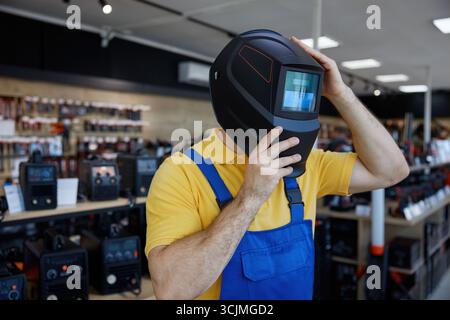 A man in a workwear wearing a protective welding helmet inside a store Stock Photo