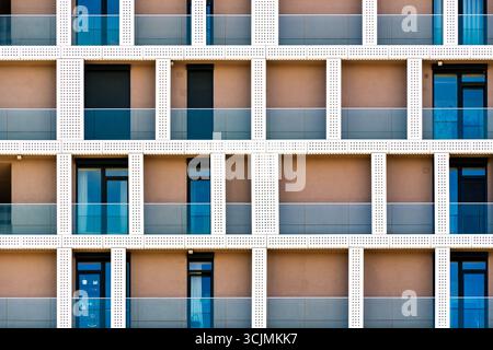 Residential building facade with glass balconies, perforated panels, and repeating geometric rhythm creating modern urban design. Stock Photo