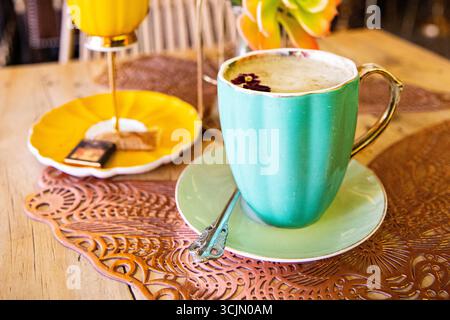 A cup of latte with a small flower in a turquoise cup Stock Photo