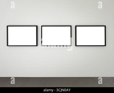 Three black rectangular picture frames mounted on a white wall above a gray floor, modern gallery mockup for displaying photography, posters, or digit Stock Photo