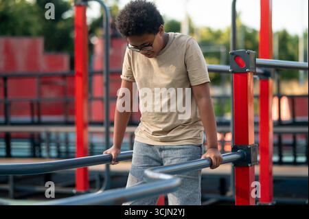 Curly-haired boy in eyeglasses spending time at the playground Stock Photo