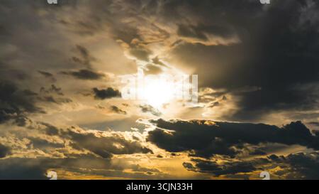 Sunset through dramatic cloudy sky with sunbeams Stock Photo