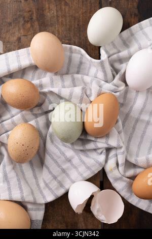 Assorted eggs and cracked shells on striped cloth over wooden table. Stock Photo