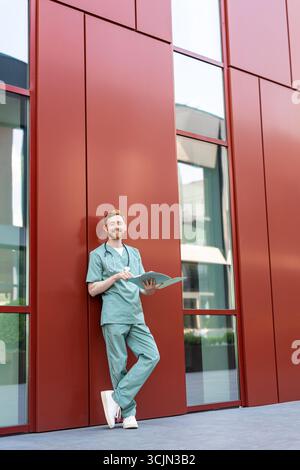 Man doctor studying papers in open medical chart near hospital building Stock Photo