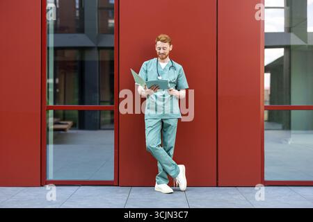 Male clinician with red hair checking open medical files outside Stock Photo