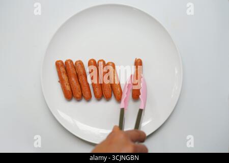 Serving Sausages with tongs on a white plate Stock Photo