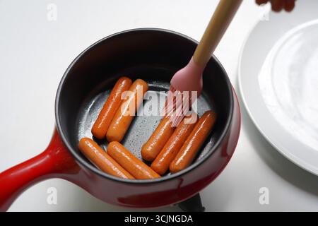 Cooking Sausages with Oil using a silicone basting brush on frying pan. Stock Photo
