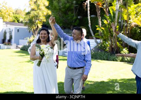 Joyful couple celebrating wedding outdoors, holding hands and smiling with guests Stock Photo