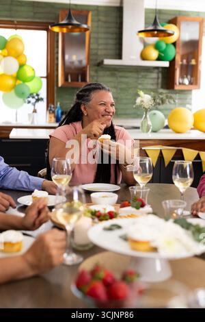 At party, senior woman having cupcake and chatting with friends Stock Photo