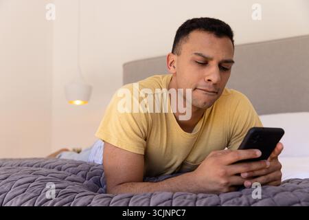 Young man lying on bed using smartphone, focused on screen Stock Photo