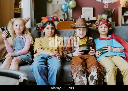 Group of Diverse Children Wearing Costumes Sitting on Sofa Playing Video Games Stock Photo