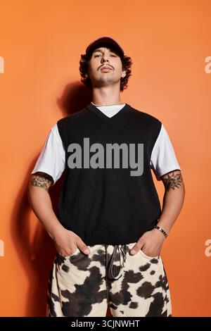 Confident young man showcases unique fashion against an orange backdrop. Stock Photo